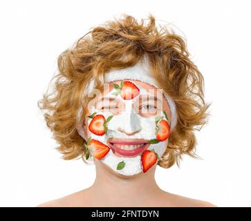 Rothaarige lockige junge Frau mit einer positiven fröhlichen Stimmung, lächelnd und zwinkert, geschlossenes Auge. Mit einer kosmetischen Maske auf dem Gesicht von Erdbeeren und Creme. Stockfoto