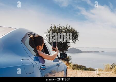 Junge Frau, die mit dem Smartphone aus dem offenen Fenster von fotografiert Ein Auto Stockfoto