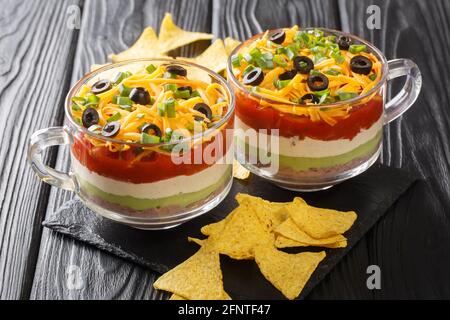 Mexikanisches Essen authentischer siebenschichtiger Dip-Salat aus Bohnenpaste, Guacamole, saurer Creme und Salsa aus nächster Nähe auf dem Tisch. Horizontal Stockfoto