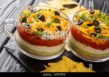 Seven-Layer Dip ist eine amerikanische Vorspeise, die auf typischen Zutaten der Tex-Mex-Küche aus nächster Nähe im Glas auf dem Tisch basiert. Horizontal Stockfoto
