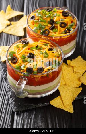 Mexikanischer siebenschichtiger Dip-Salat, serviert mit Chips aus nächster Nähe auf dem Tisch. Vertikal Stockfoto