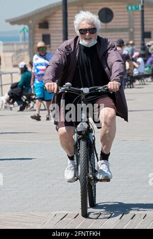 Ein älterer Mann mit weißen Haaren und einem Spitzbart fährt auf dem Boardwalk in Coney Island, Brooklyn, New York City, mit dem Fahrrad. Stockfoto