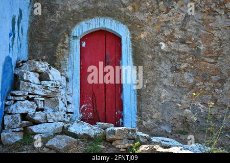 Altes ländliches Haus, rote gewölbte Holztür auf einer verwitterten handgefertigten Steinmauer in Perlegkianika, Kythira Insel Attica Griechenland. Stockfoto