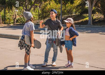 Drei kaukasische Eislaufkinder, die in legerer und urbaner Kleidung gekleidet sind, begrüßen sich nach einem Treffen in einem Skatepark glücklich. Stockfoto