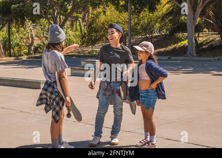 Drei kaukasische Eislaufkinder, die in legerer und urbaner Kleidung gekleidet sind, begrüßen sich nach einem Treffen in einem Skatepark glücklich. Stockfoto