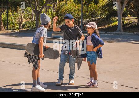 Drei kaukasische Eislaufkinder, die in legerer und urbaner Kleidung gekleidet sind, begrüßen sich nach einem Treffen in einem Skatepark glücklich. Stockfoto
