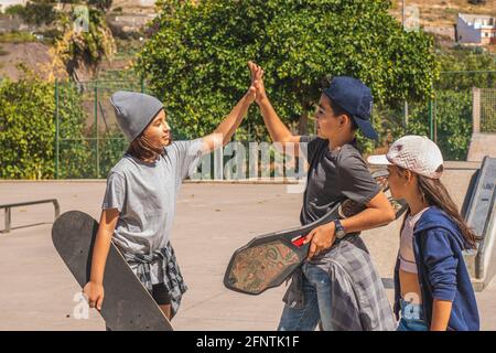 Drei kaukasische Eislaufkinder, die in legerer und urbaner Kleidung gekleidet sind, begrüßen sich nach einem Treffen in einem Skatepark glücklich. Stockfoto