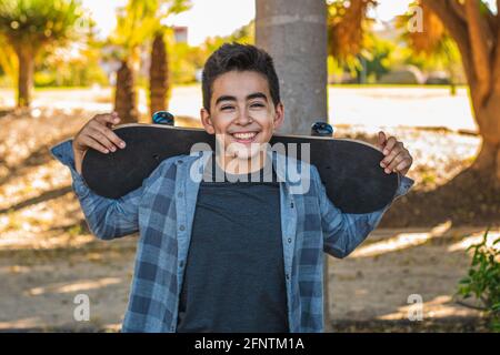 Porträt eines kaukasischen Skater Jungen, der die Kamera anschaut, mit ihrem Skate, der in einem Skatepark sehr lächelt Stockfoto