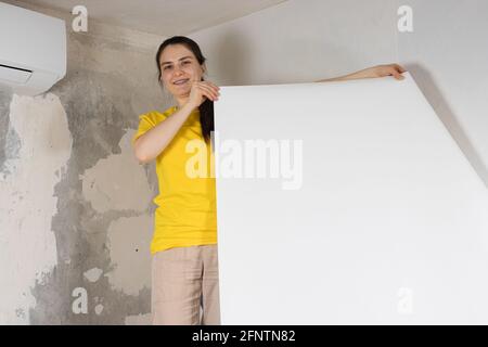 Eine Reparaturfrau klebt weiße Tapeten an der Wand in der Nähe Die Klimaanlage unter der Decke Stockfoto