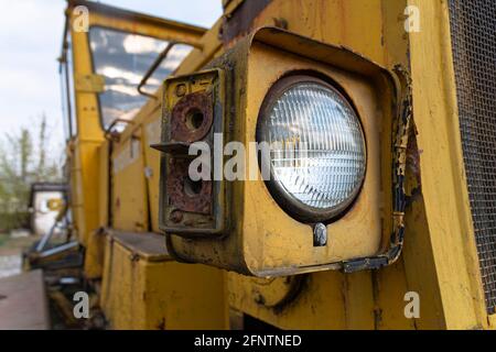 Scheinwerfer einer alten verlassenen kaputten Straßenbaumaschine (Grader). Rostiges Metall, zerbrochenes Glas und die Reste der alten Farbe. Stockfoto