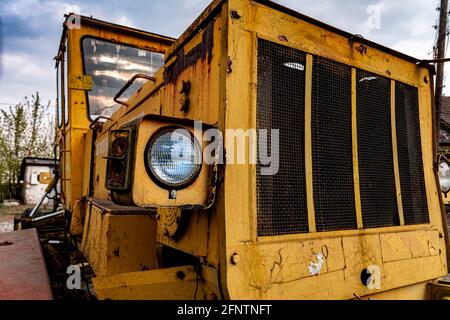 Scheinwerfer und Vorderteil einer alten verlassenen kaputten Straßenbaumaschine (gelber Motorgrader). Rostiges Metall, zerbrochenes Glas und die Reste von alt Stockfoto