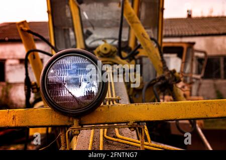 Scheinwerfer und Vorderteil einer alten verlassenen kaputten Straßenbaumaschine (Grader). Rostiges Metall, zerbrochenes Glas und die Reste der alten Farbe. Stockfoto