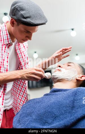 Friseur etwas Rasierschaum auf einem Client vor der Rasur, sein Bart in einem Friseur Stockfoto