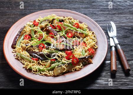 Auberginen-Nudelsalat mit grünen Bohnen auf einer Steingutplatte auf einem dunklen rustikalen Holztisch, horizontale Ansicht von oben Stockfoto