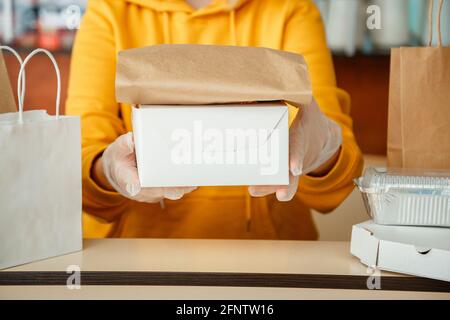 Der Kellner gab Essen zum Mitnehmen, während die Stadt um 19 Uhr gesperrt wurde, das Coronavirus wurde heruntergefahren. Backen zum Mitnehmen, Pizzakaffee zum Mitnehmen, Lieferung von Lebensmitteln. Frau in Handschuhen Stockfoto