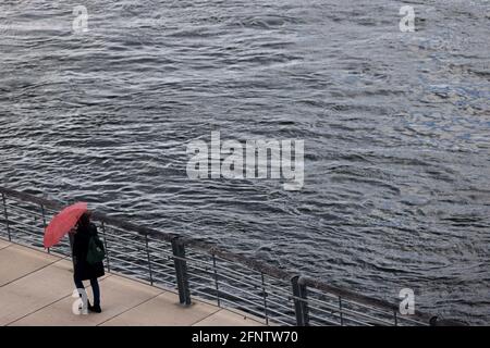 Köln, Deutschland. Mai 2021. Eine Frau mit einem Sonnenschirm läuft am Rheinufer entlang. Quelle: Oliver Berg/dpa/Alamy Live News Stockfoto