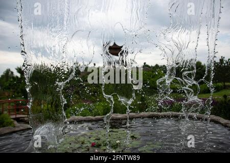 Wasserfall gegen den Himmel. Das fallende Wasser ist im Bild gefroren. Kühle Aufnahme von Wasserspritzern. Stop Rahmen eines kleinen Wasserfalls in einem Park. Stockfoto