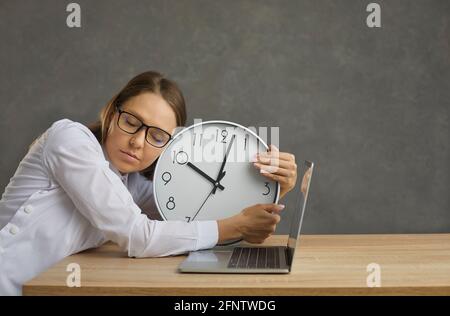 Freiberuflicher Mitarbeiter, der bei der Arbeit schläft, umarmt die Uhr an der Rezeption Des Laptops Stockfoto