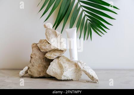 Natürliche Schönheit kosmetische Tube Mockup Produkt für Hautpflege mit Palmblatt-Pflanze auf Stein Sockel grauen Hintergrund. Natürlicher Gesteinsstapel aus balancierenden Steinen Stockfoto