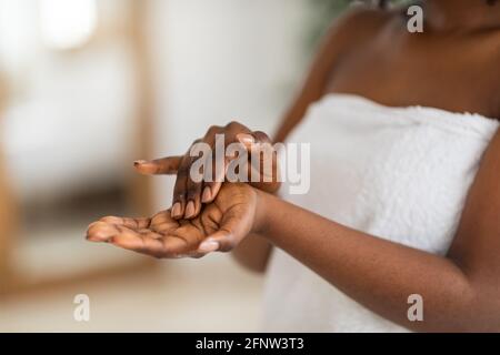 Beschnittene Ansicht einer jungen schwarzen Frau, die zu Hause feuchtigkeitsspendende Handcreme in Nahaufnahme anwendet Stockfoto