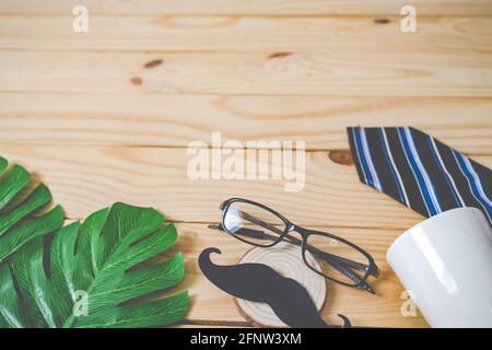 Blur of Background, Happy Father's Day Konzept. Ein schwarzes Schnurrbart-Papier, eine blaue Krawatte, eine blaue Geschenkbox und Gläser auf einem Holztisch. Stockfoto