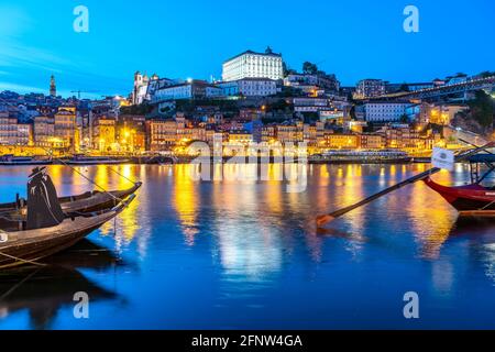 Blick über die traditionellen Rabelo Boote am Douro Ufer in Vila Nova de Gaia auf die Altstadt von Porto in der Abenddämmerung, Vila Nova de Gaia, Po Stockfoto