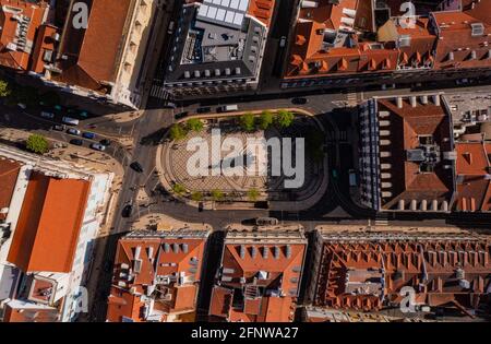 Blick von oben auf den Marktplatz in Lissabon, Portugal. Dekorativer gefliester Boden mit Ornamenten und Statue auf achteckigem Sockel, der mit einer Straße gesäumt ist. Stockfoto
