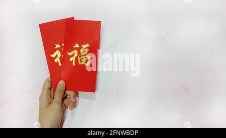 Eine Hand, die zwei Angpau hält, rote Päckchen mit Geld im Inneren, die als Segen in der chinesischen Kultur, besonders während des chinesischen Neujahrs, gegeben werden. Stockfoto