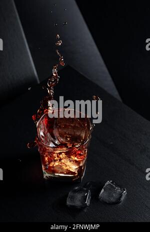 Eiswürfel fallen in ein Glas Whiskey und erzeugen Spritzer. Stockfoto