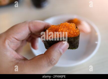 Gunkan Sushi aus Tobiko fliegender Fischrogen in der Hand mit dezenter Beleuchtung in Innenräumen. Stockfoto