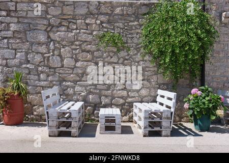 Bänke befinden sich unter Grün vor einem historischen Steinmauer zwischen zwei Blumentöpfen Stockfoto