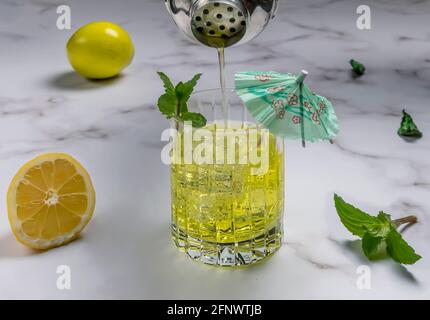 Ein Cocktail aus Zeder-, Zitronen- und Minzblättern wird aus dem Mixer in einen Glasbecher auf einem Marmortisch gegossen Stockfoto