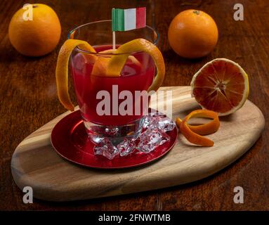 Ein Glas frisch gepresster Orangensaft mit dem Italiener Flagge auf ihm neben Orangen und Eiswürfeln Stockfoto
