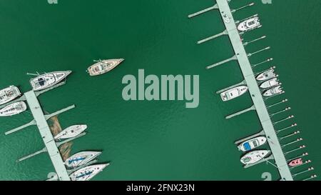 Luftaufnahme einer Menge weißer Yachten und Segelboote, die in der Marina auf einem türkisfarbenen Wasser festgemacht sind, im Frühling. Stockfoto