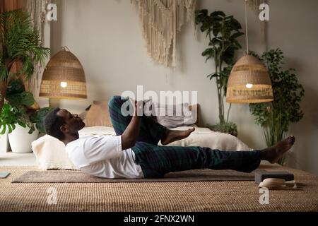 Afrikanischer Mann, der Yoga auf dem Boden macht und die unterstützte, einbeinige Wind-lindernde Pose übt Stockfoto