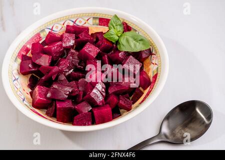 Rübensalat mit Olivenöl und Basilikum auf einem Teller auf weißem Marmorboden. Frisches und gesundes Gemüse Konzept. Stockfoto