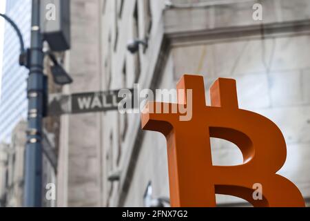 Ein Modell eines Bitcoins wird neben einem Wall Street-Schild in Downtown Manhattan gehalten, das die Beziehung zwischen traditionellem Finanzwesen und Bitcoin zeigt. Stockfoto