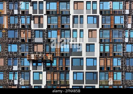 Ein buntes Fragment der Fassade eines im Bau befindlichen mehrstöckigen Gebäudes, dessen Isolierung mit mineralischer Isolierung mittels einer Winde. Stockfoto