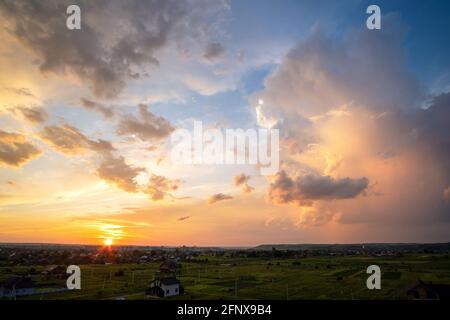 Dramatischer Sonnenuntergang über der ländlichen Gegend mit stürmischen geschwollenen Wolken, die von orangefarbenem Sonnenuntergang und blauem Himmel beleuchtet werden. Stockfoto