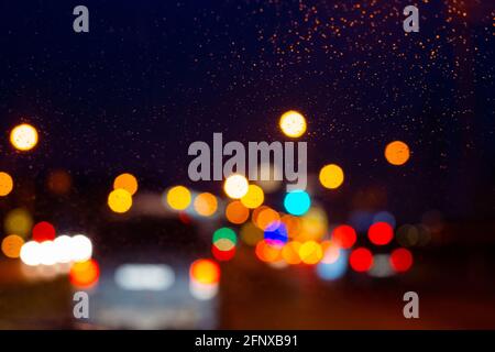Verschwommene mehrfarbige Lichter der Beleuchtung auf einem Autoglas an einem regnerischen Abend, verschwommener Hintergrund, Kopierraum Stockfoto
