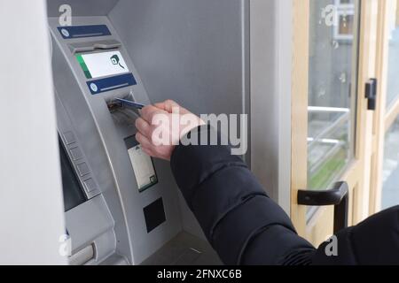 Eine Männerhand legt eine Kreditkarte in einen Geldautomaten ein. Stockfoto