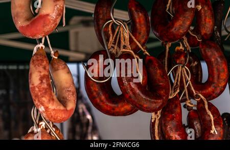 Typische spanische Würste hängen an einem Dorfstand am Lebensmittelmarkt, traditionelle Fleischprodukte Stockfoto