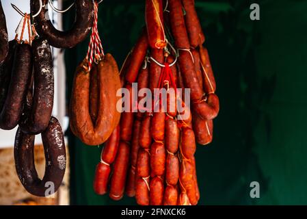 Typische spanische Würste hängen an einem Dorfstand am Lebensmittelmarkt, traditionelle Fleischprodukte Stockfoto