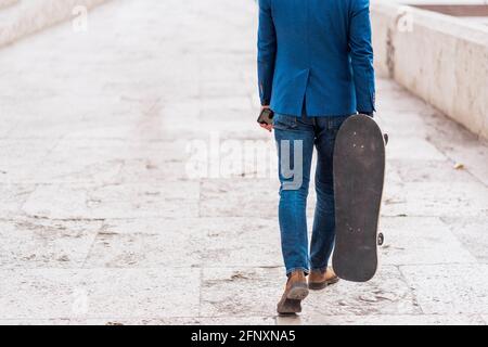 Ein selbstbewusster Geschäftsmann hält Skateboard und spaziert durch die Stadt Brücke Stockfoto