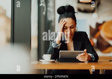 Eine Latina-Frau sitzt in einem Café und schaut hinein Enttäuschung über das Tablet Stockfoto