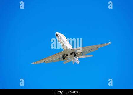 Flugzeug am Himmel bei Sonnenaufgang oder Sonnenuntergang. Kleiner Business Jet mit Landescheinwerfer und eingesetztem Fahrwerk zur Vorbereitung auf die Landung am Flughafen. Stockfoto