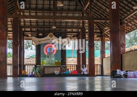 Sri-lankische Menschen chillen an einem ruhigen Ort der Kontemplation neben einer buddha-Statue, umgeben von bunten Neonlichtern, Anuradhapura, Sri Lanka Stockfoto