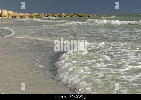Nahaufnahme von sanfter Brandung, die sich am Strand von Marco Island, Florida, ausbreitet, aufgenommen aus einem niedrigen Winkel bei weichem Licht mit einem Steinpier in der Ferne sichtbar Stockfoto