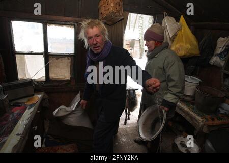 Weißrussland. Malye Volneiki Dorf - 28,11,2010: Ein älterer Mann und eine ältere Frau in einem alten Dorfhaus mit einer offenen Tür im Hintergrund. Stockfoto