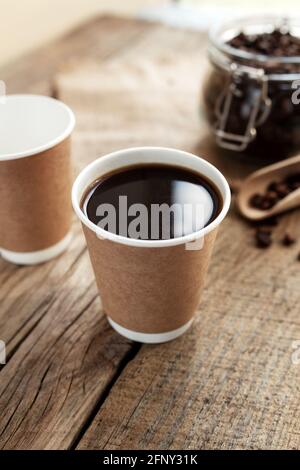 Pappbecher Kaffee, trockene Kaffeebohnen im Glas und Löffel am Holztisch Stockfoto